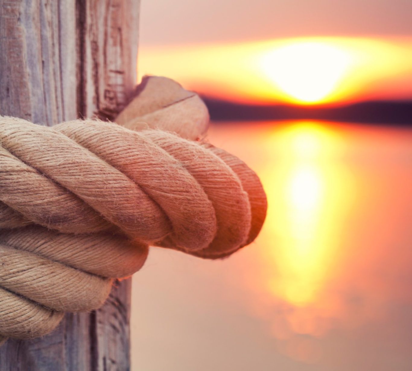 Holzpfeiler mit dickem Tau und Sonnenaufgang.