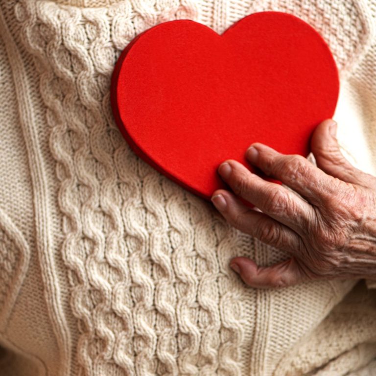 Seniorin hält sich ein Herz aus Holz vor die Brust.